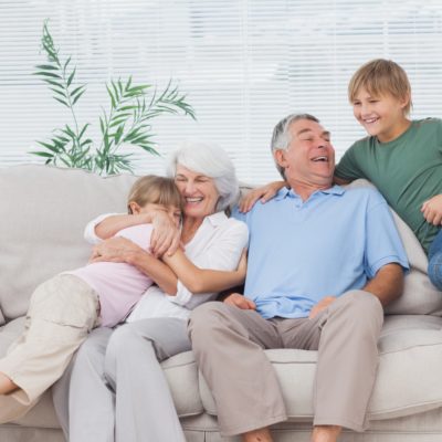 Smiling grandchildren embracing their grandparents on couch
